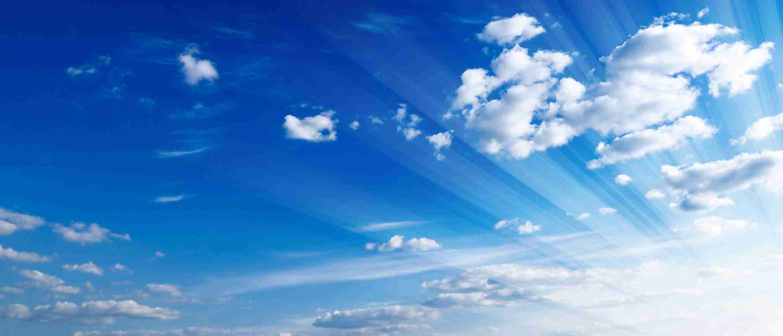 Expansive blue sky with sunbeams piercing through fluffy white clouds.