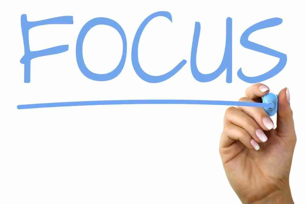 Hand writing the word "focus" with a blue marker on a clear surface or in mid-air, emphasizing the concept of concentrating on a task or goal.