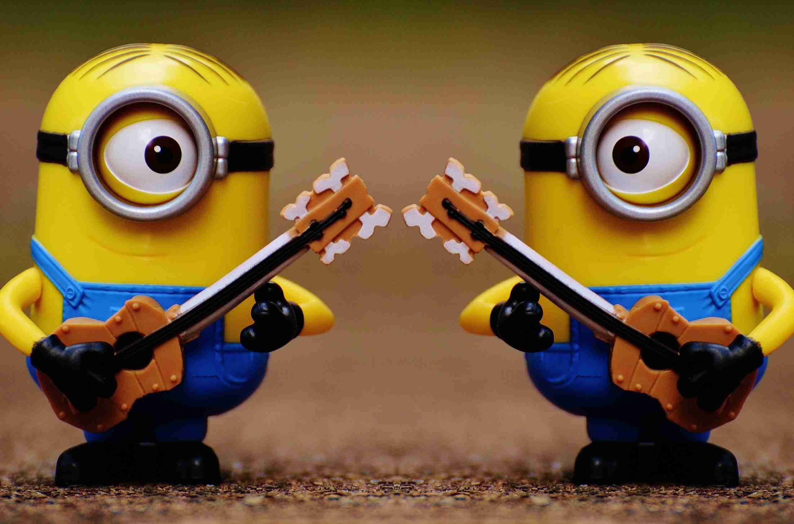 Two minion toys facing each other, each holding a guitar as if in a musical duel.