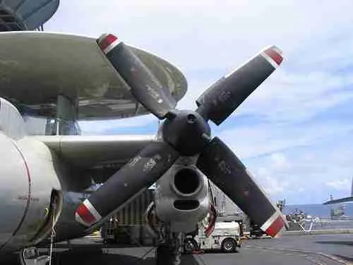 A close-up view of an aircraft's turboprop engine with its good propeller blades, under the wing of the plane, set against a cloudy sky.